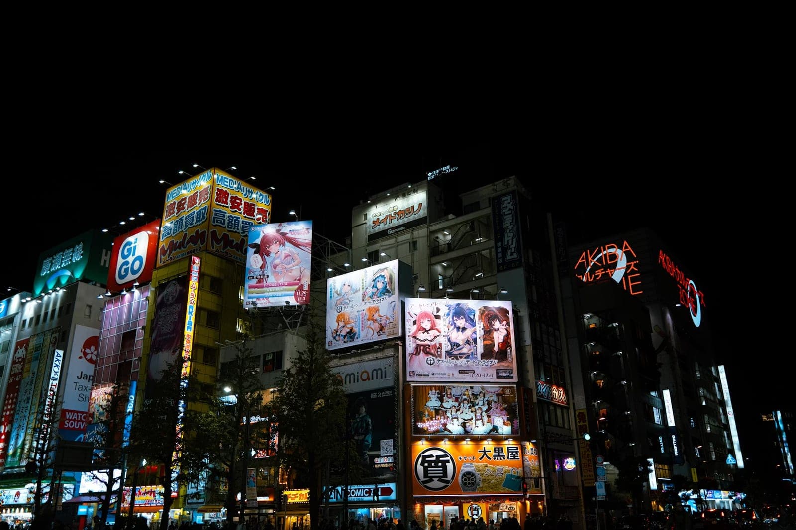Edificios de Akihabara de noche cubiertos de anuncios luminosos de anime, con el letrero de neón Akiba Culture Zone