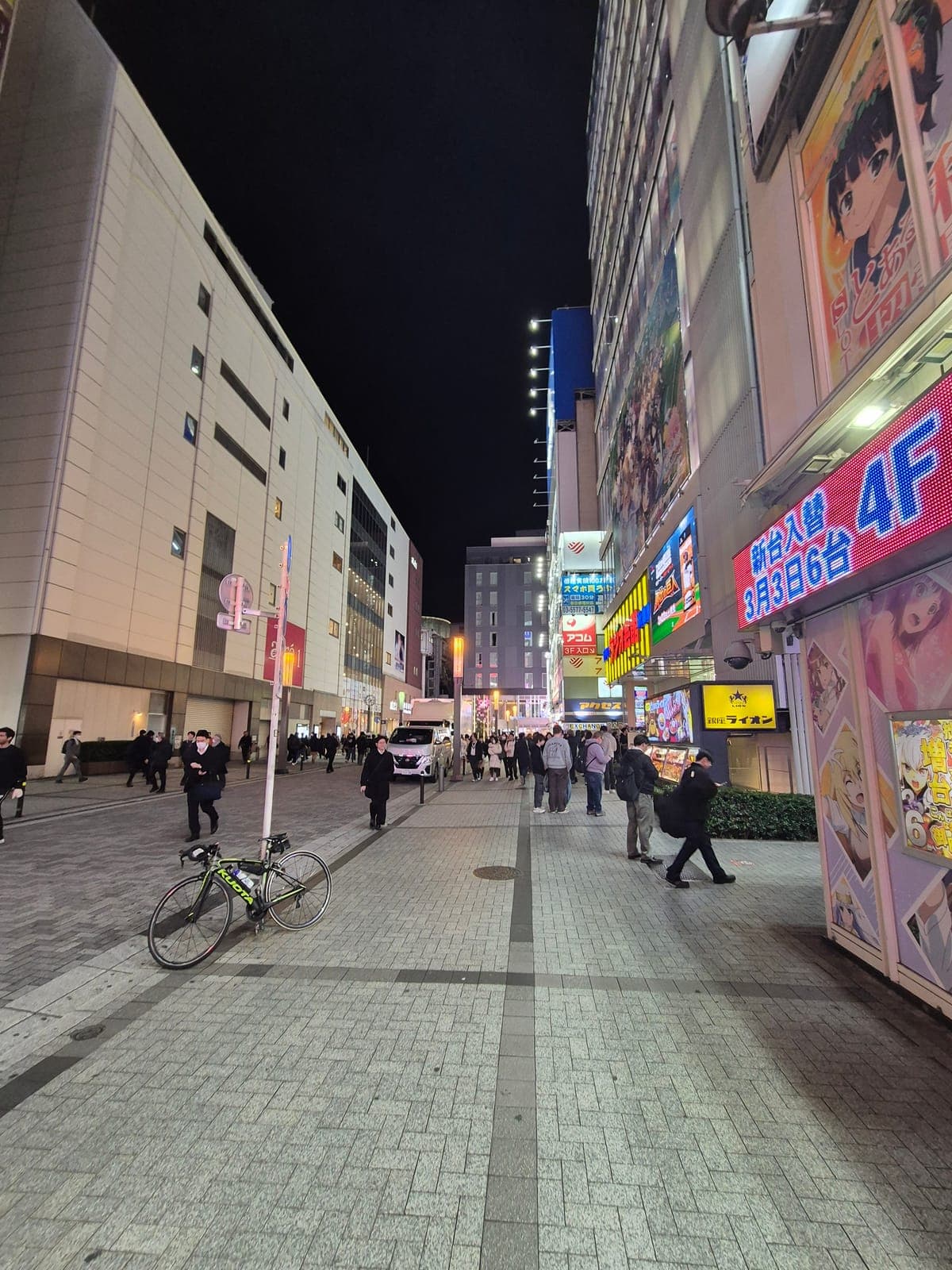 Calle de Akihabara de noche con letreros luminosos de anime y peatones frente a las tiendas