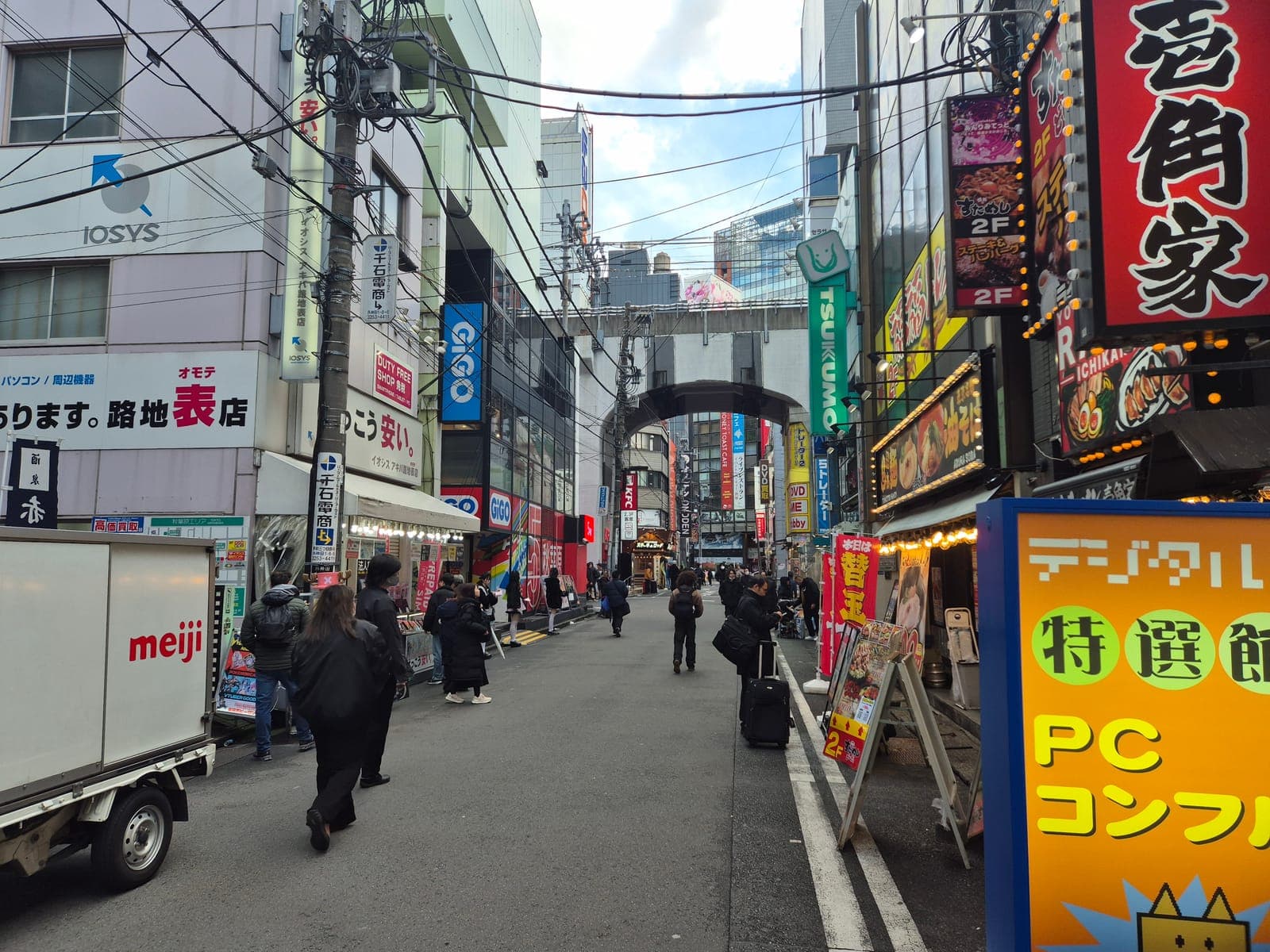 Calle lateral de Akihabara junto a las vías del tren, con letreros de GiGO, restaurantes de ramen y tiendas de electrónica