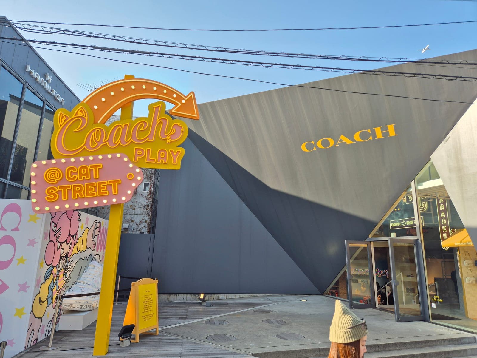 Letrero de Coach Play en Cat Street, Harajuku, junto a un edificio de fachada geométrica y una tienda Coach