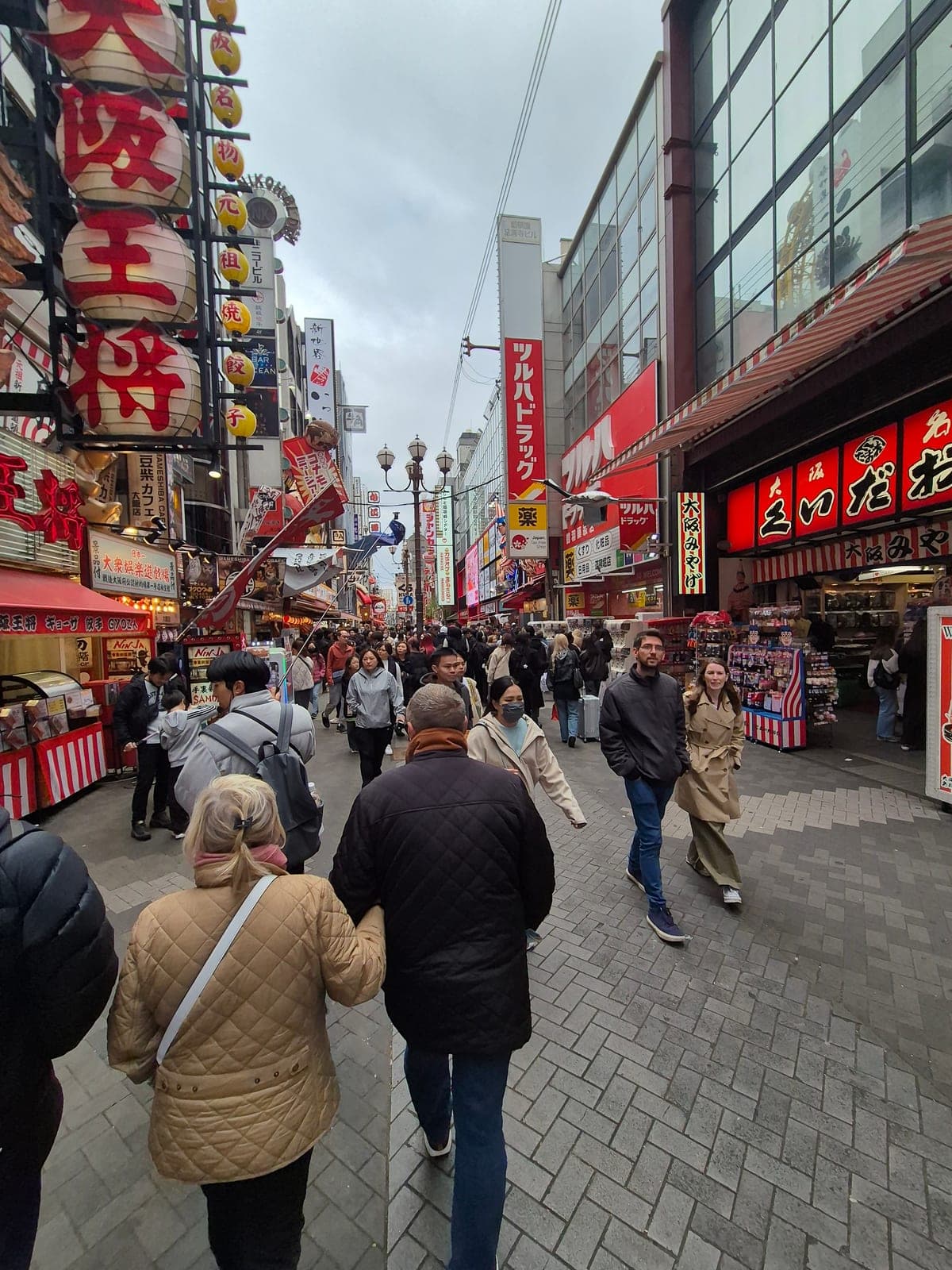 Calle comercial de Dotonbori en Osaka de día, con letreros y farolillos rojos colgando sobre los locales y gente caminando entre las tiendas