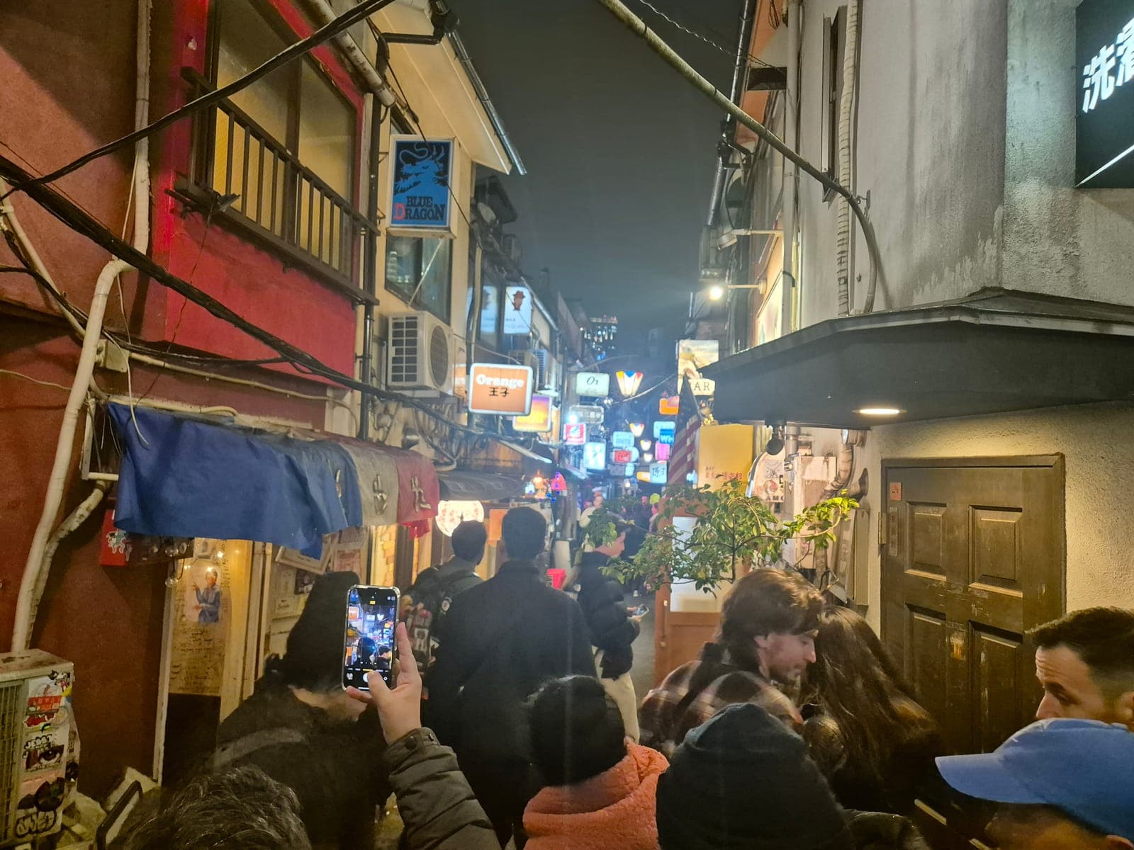 Callejón muy angosto de Golden Gai en Shinjuku de noche, con decenas de letreros de bares apilados y gente caminando apretada
