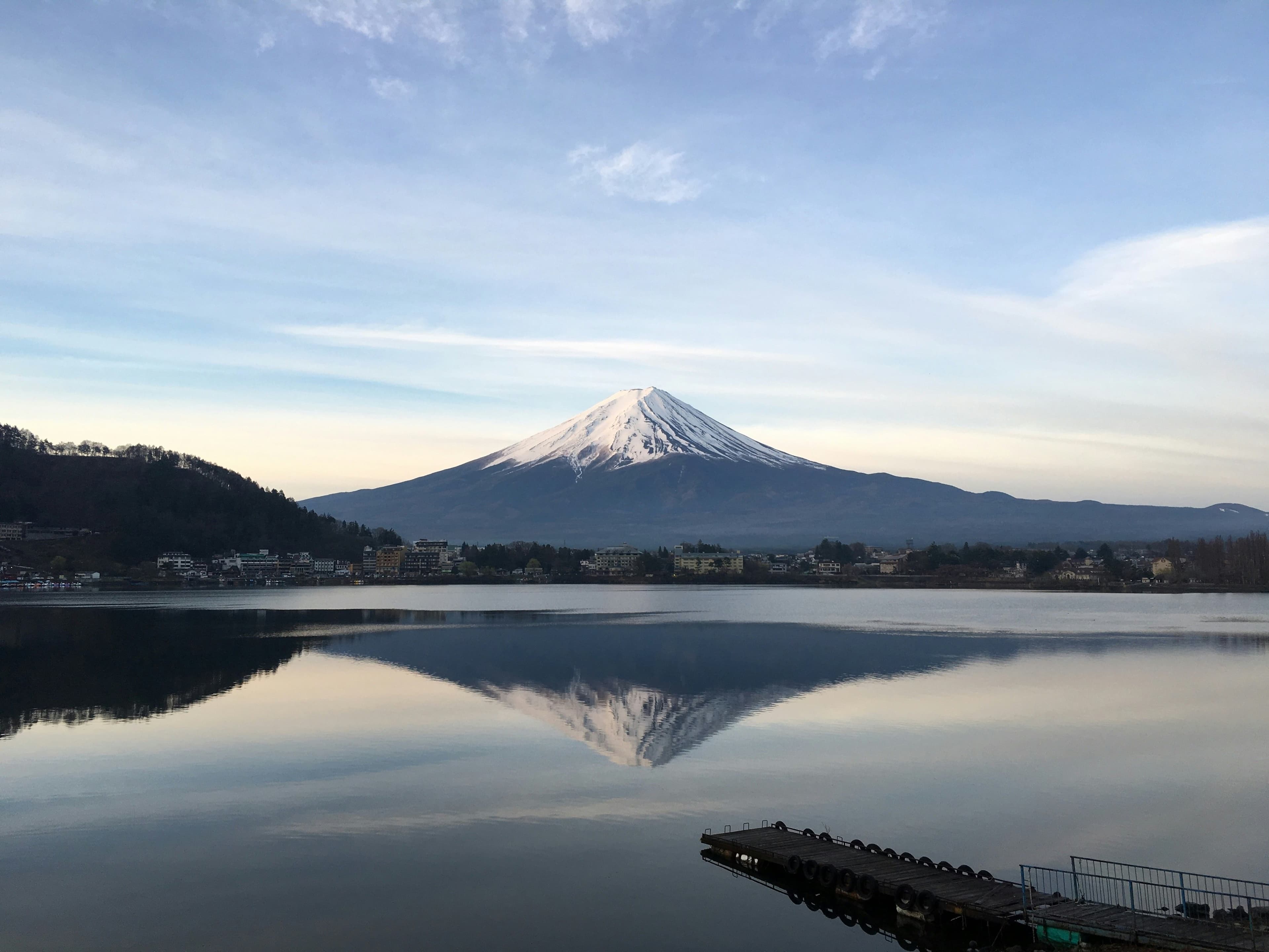 El Monte Fuji nevado reflejado en el agua del lago Kawaguchiko, con un muelle de madera en primer plano