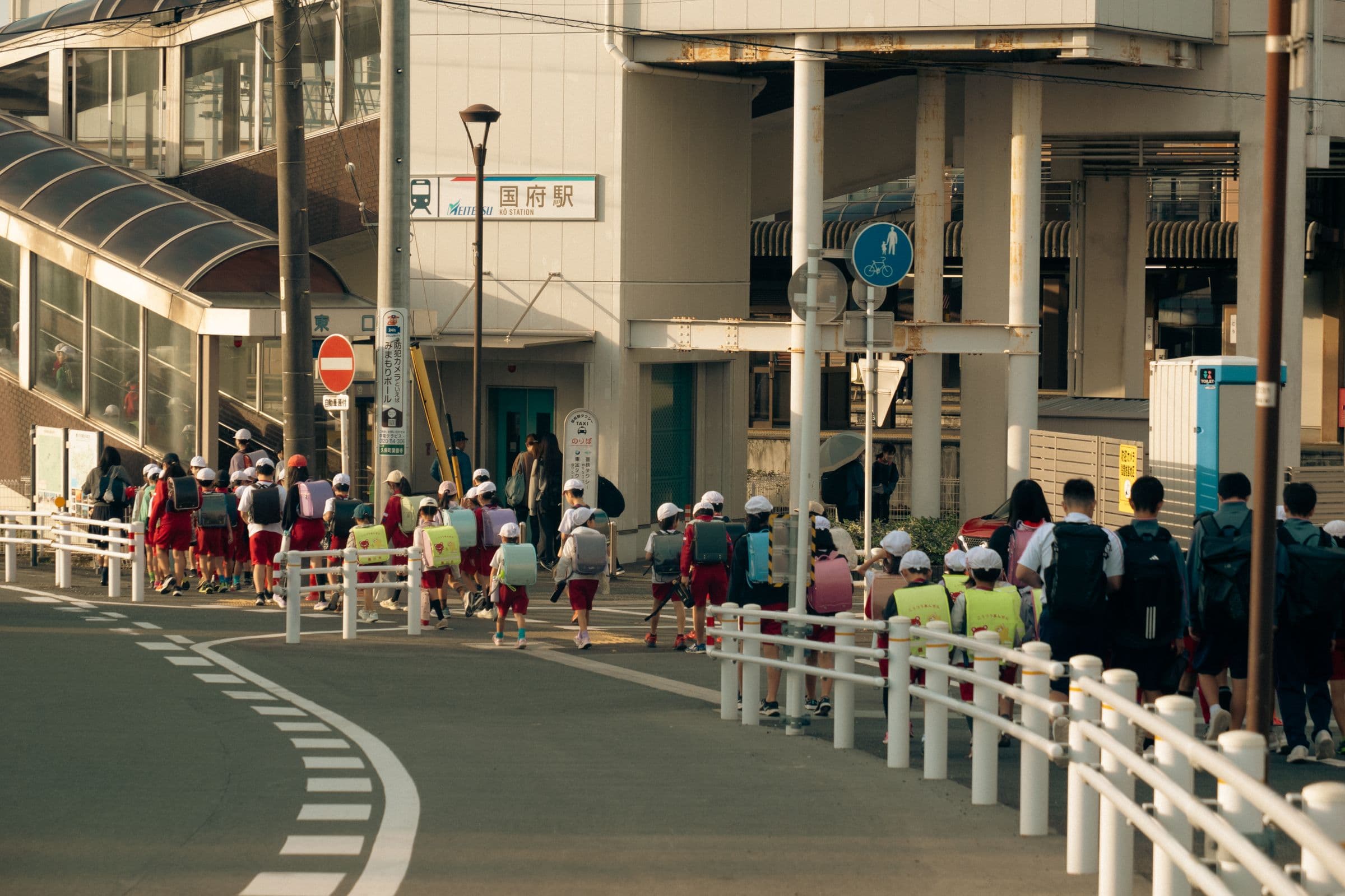 Estudiantes con mochilas caminando junto a la estación de tren de Kokufu, en Japón, con el letrero de la estación al fondo