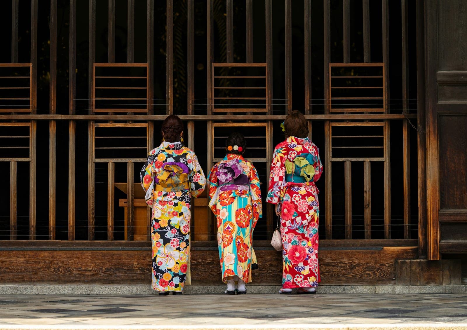 Tres mujeres en kimonos de colores, de espaldas, frente a la puerta de madera de un templo de Kioto