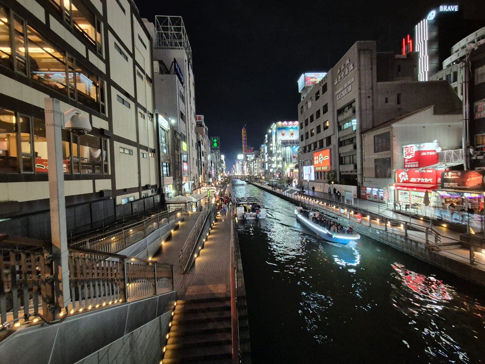 El canal de Dotonbori de noche, con un barco turístico iluminado navegando entre edificios cubiertos de anuncios de neón como Kirin y Kobe Beef