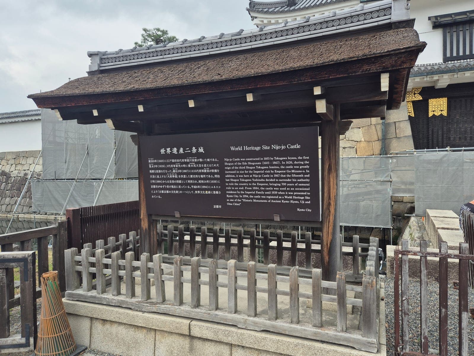 Letrero bilingüe de Patrimonio de la Humanidad del castillo Nijō en Kioto, con el muro de piedra y la puerta de entrada al fondo