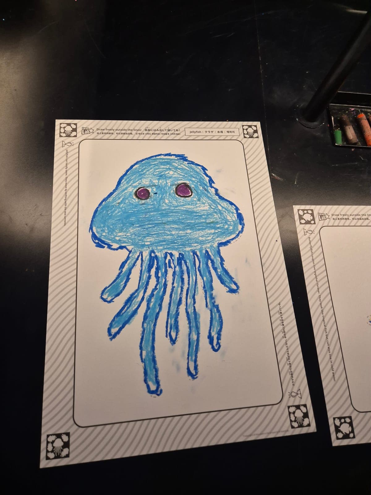 Dibujo infantil de una medusa azul a crayón sobre una hoja de la actividad Sketch Ocean de teamLab Borderless