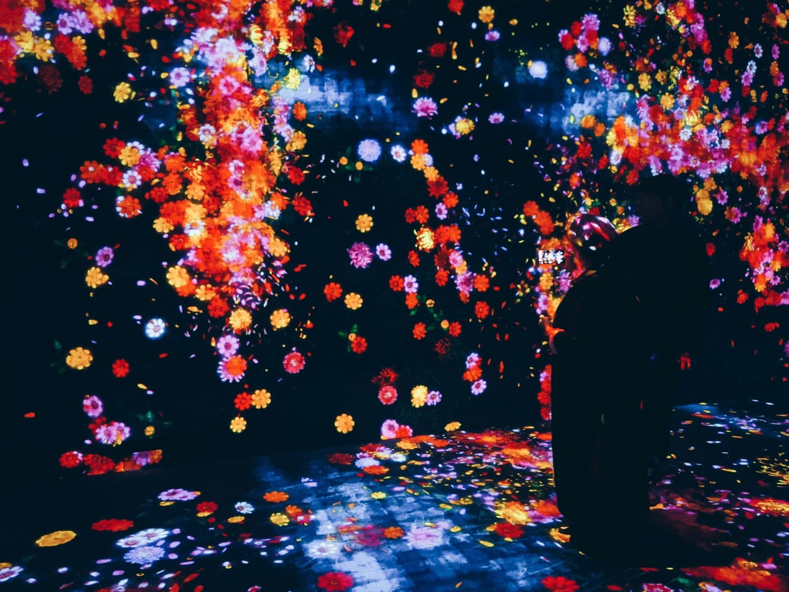 Uno de los tramos de The Way of the Sea en teamLab Borderless, con una lluvia de flores proyectadas en tonos naranja y rosa cubriendo el techo y el piso