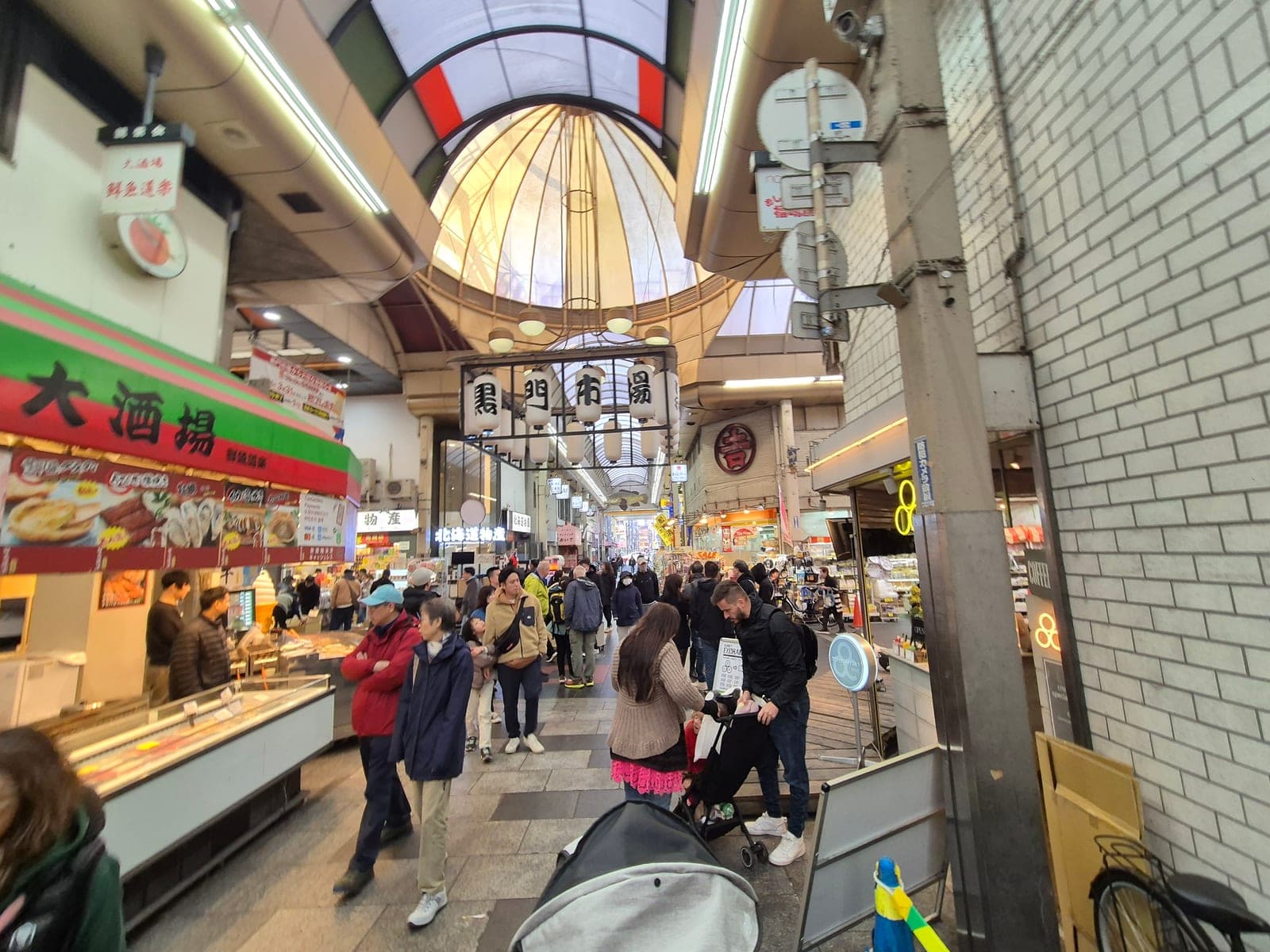 El pasillo techado del mercado Kuromon Ichiba en Osaka, con puestos de comida a ambos lados y gente comprando