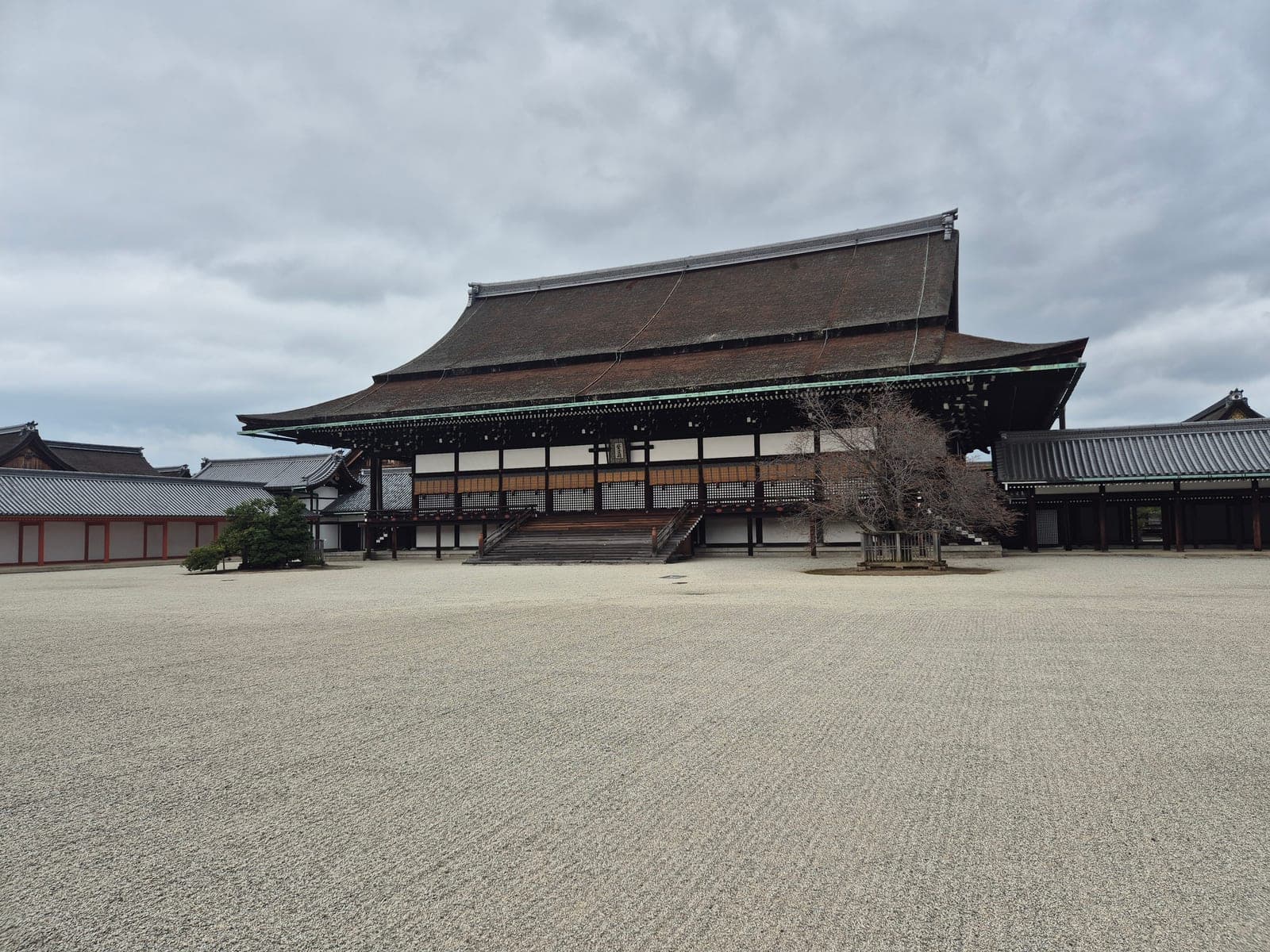 El salón Shishinden del Palacio Imperial de Kioto visto de frente, con su tejado curvo de corteza sobre una explanada de grava, bajo un cielo nublado