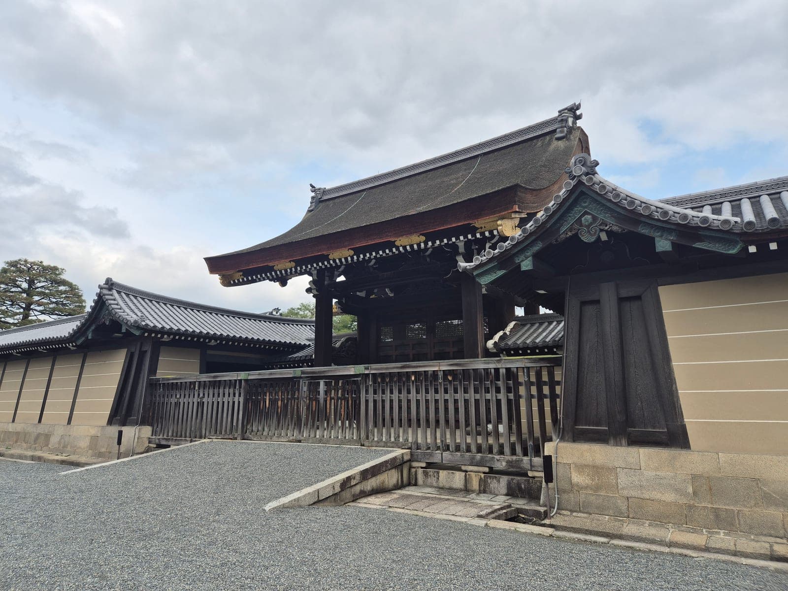La puerta Gishūmon del Palacio Imperial de Kioto, con techo curvo de corteza y herrajes verdes patinados, bajo un cielo nublado