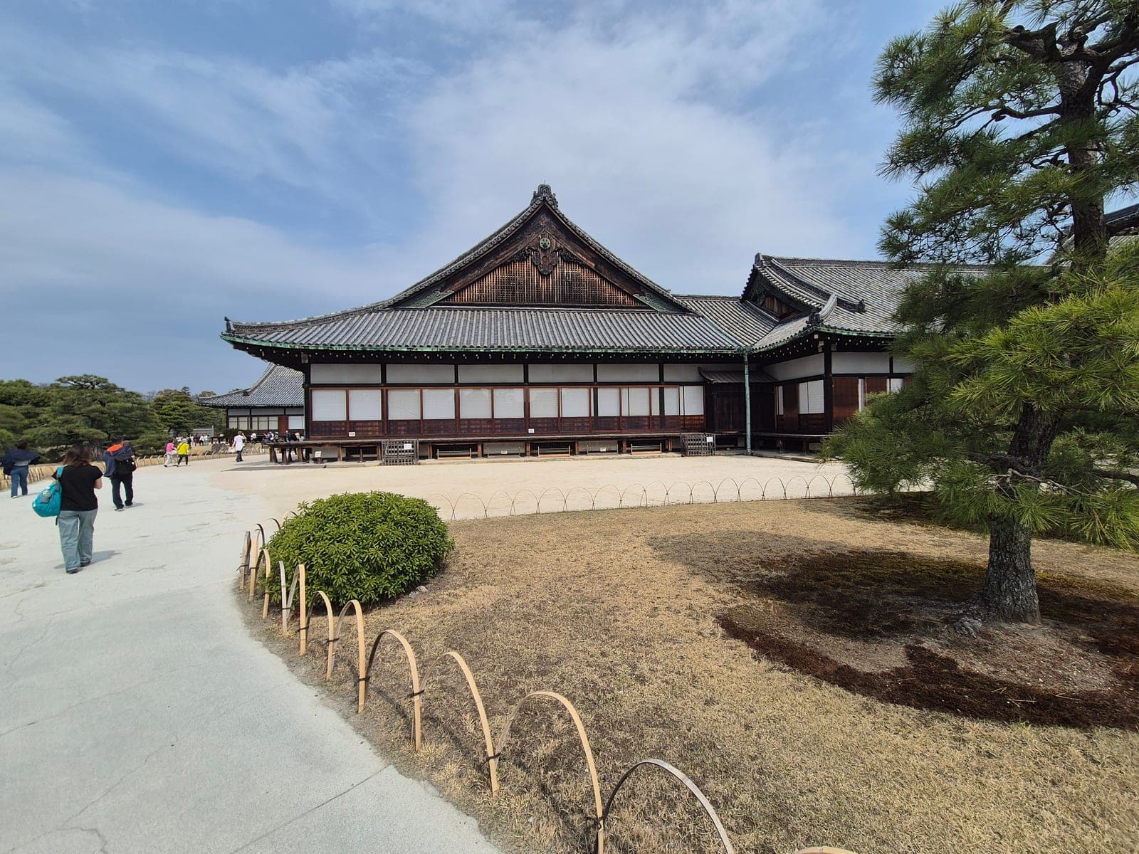 Fachada del palacio Ninomaru en el castillo Nijō, con techo de tejas grises, aleros de madera oscura y un pino junto a la entrada