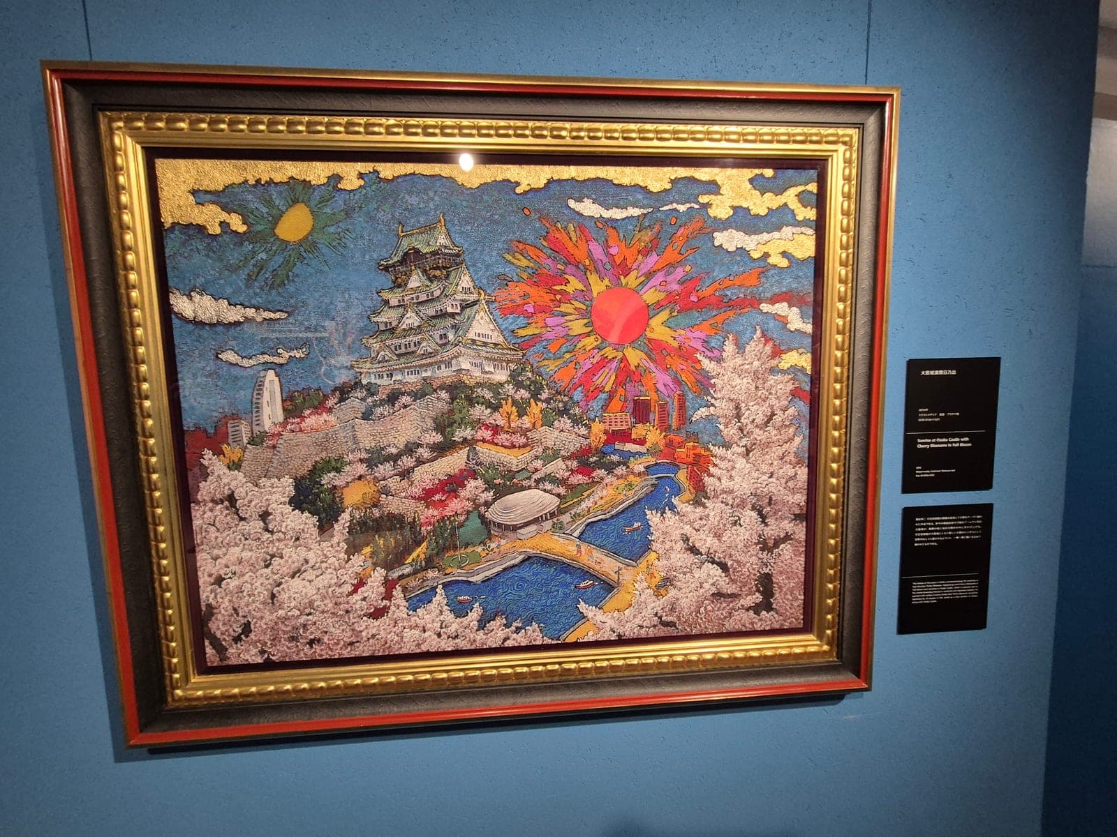 Pintura de Koji Kinutani que muestra un amanecer sobre el Castillo de Osaka rodeado de flores de cerezo, con un sol estilizado en tonos rosas y dorados