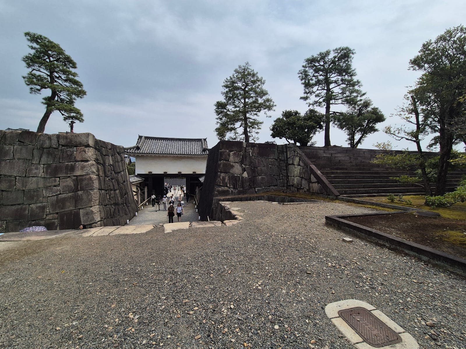 Sendero de piedra hacia la puerta Honmaru Yagura-mon del castillo Nijō, entre murallas altas y pinos
