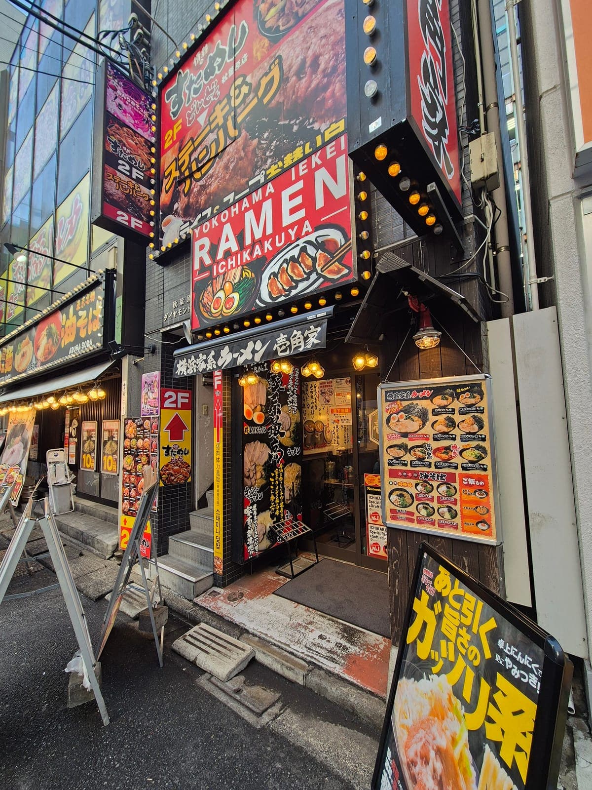 Entrada del restaurante de ramen Ichikakuya en Akihabara, cubierta de letreros iluminados y fotos del menú