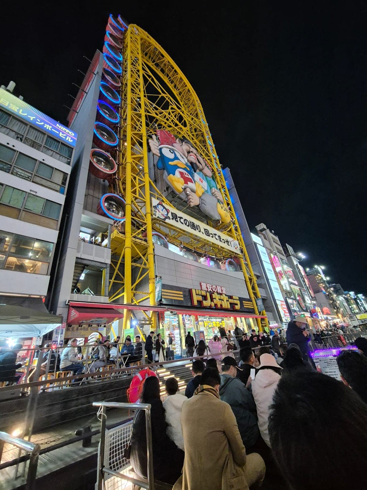 La rueda de la fortuna de la Ebisu Tower sobre la tienda Don Quijote en Dotonbori, iluminada de noche junto a una mascota gigante en forma de pez globo