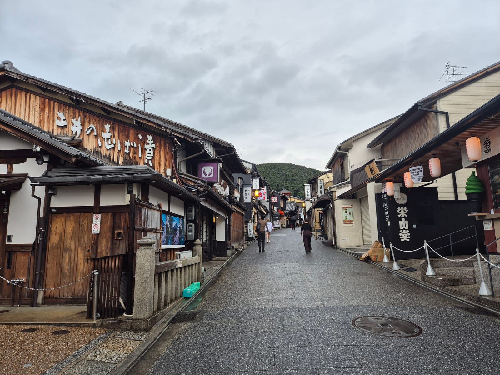 La calle empedrada de Sannenzaka en Kioto, con tiendas tradicionales de madera, farolillos y turistas caminando bajo un cielo nublado