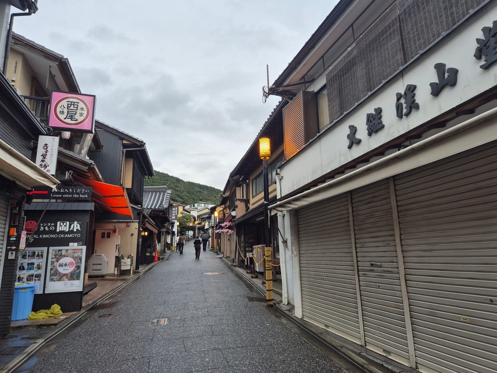 Tienda de yatsuhashi Nishio con su letrero circular rosa en una calle de Higashiyama, junto a un local de renta de kimonos, en Kioto