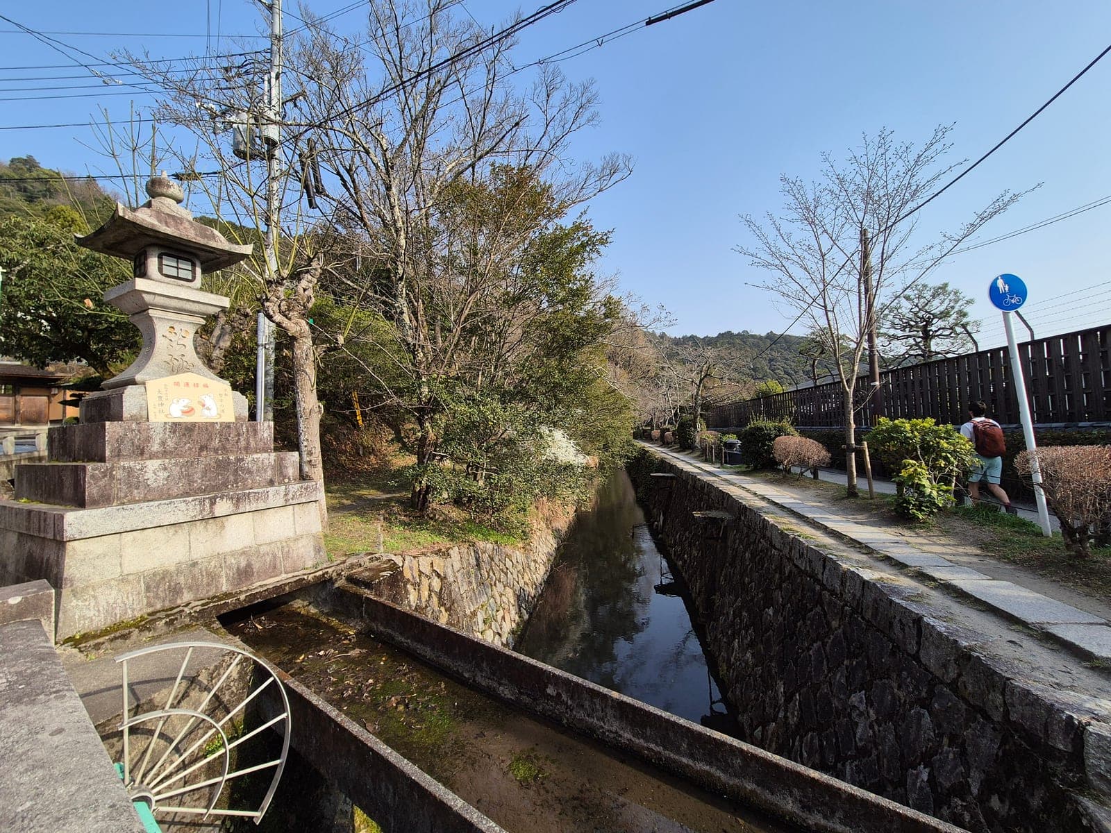 Un farol de piedra junto al canal del Paseo del Filósofo, con un letrero de bienvenida al santuario Otoyo ilustrado con ratones