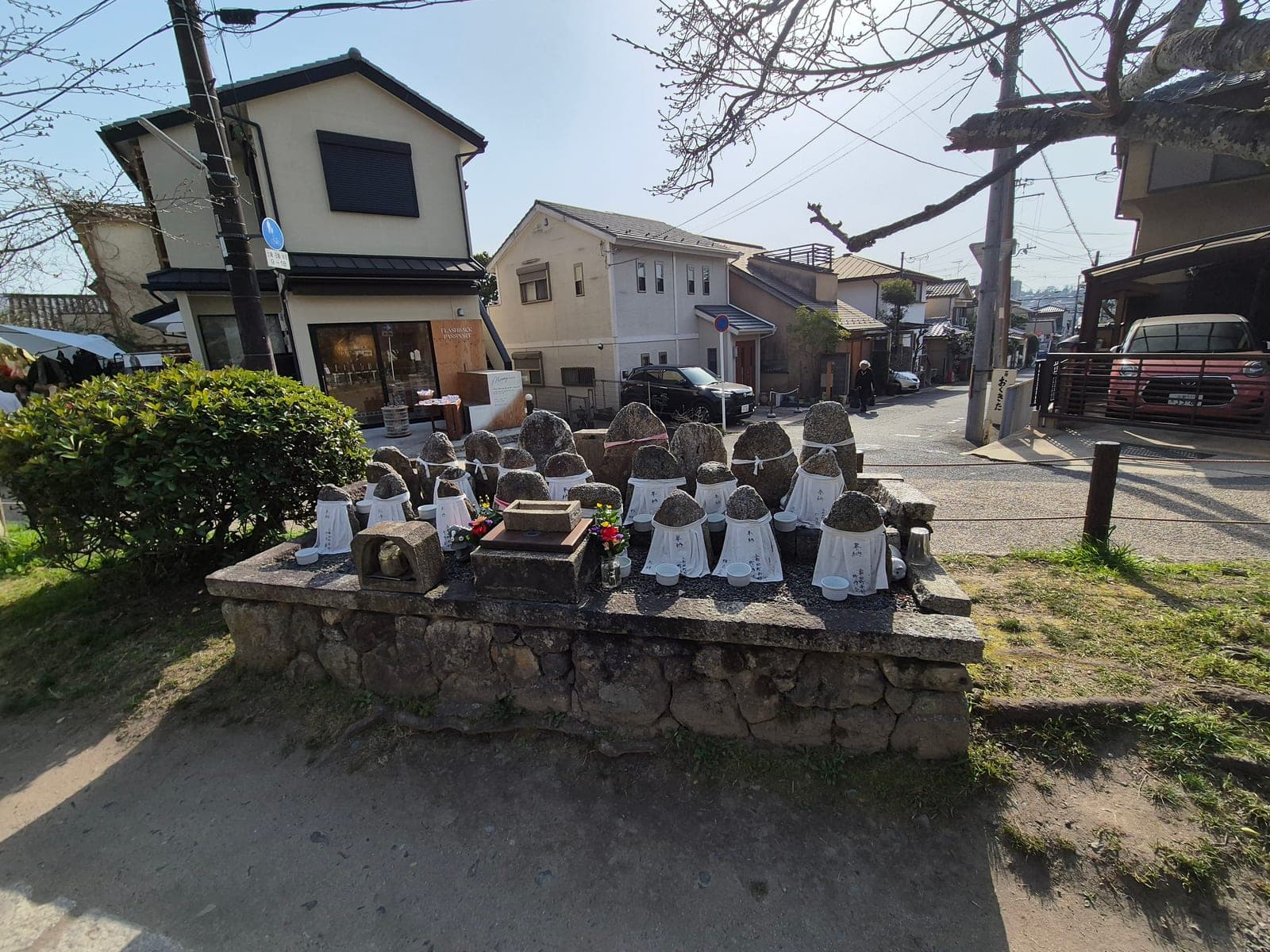Un grupo de pequeñas estatuas de piedra Jizō con bandas blancas de tela, ofrendas y flores, en una esquina cerca del Paseo del Filósofo en Kioto