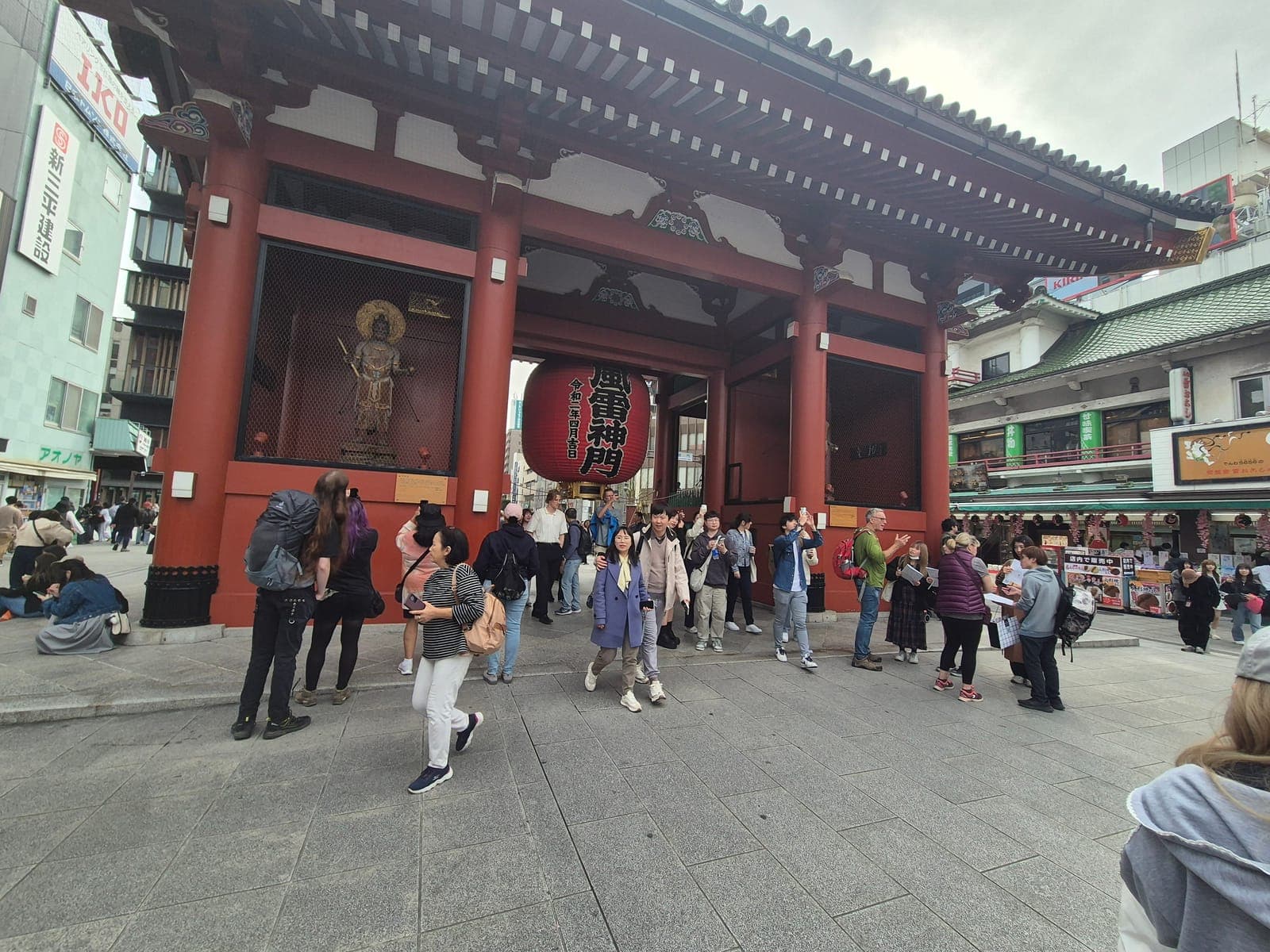 La puerta Kaminarimon del templo Sensō-ji con su farol rojo gigante y la estatua de uno de los dioses guardianes, rodeada de visitantes