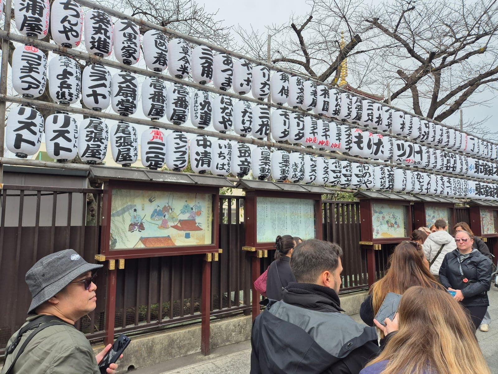 Hileras de linternas de papel blancas sobre paneles pintados al estilo Edo que ilustran la historia del templo Sensō-ji