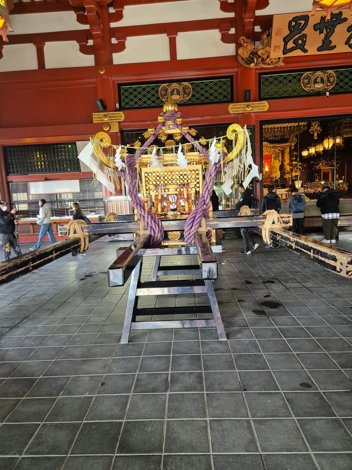 Un mikoshi dorado, altar portátil con cuerdas moradas y vigas de madera negra, exhibido dentro del salón principal del Sensō-ji