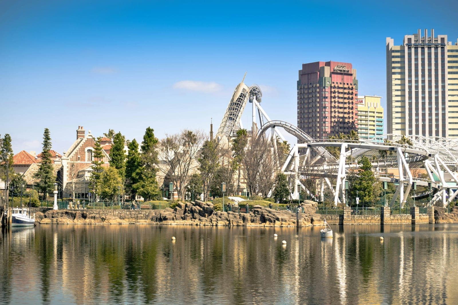 La vía blanca de la montaña rusa Hollywood Dream The Ride serpenteando sobre los edificios de Universal Studios Japan, vista desde la laguna del parque con los hoteles de Universal City al fondo