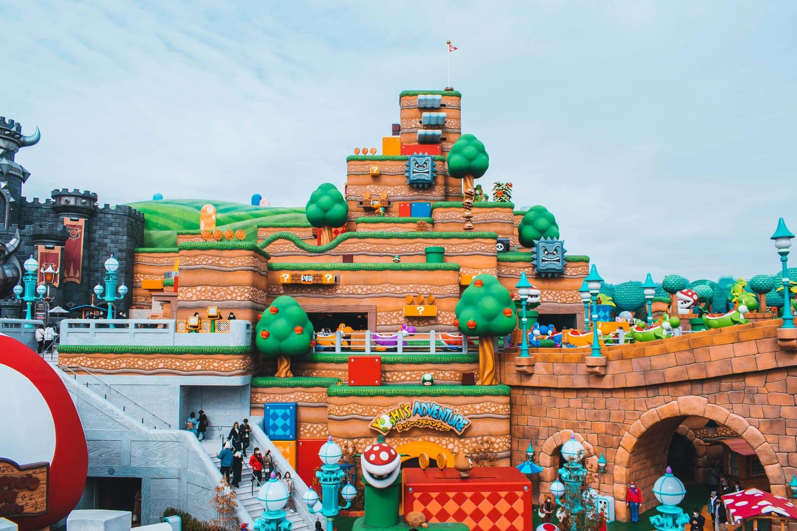 El interior de Super Nintendo World en Universal Studios Japan, con la montaña de bloques de Yoshi's Adventure, árboles y enemigos del videojuego, y el Castillo de Bowser asomando a la izquierda