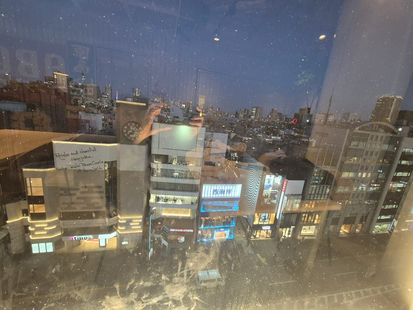 Vista nocturna de los edificios y letreros de Harajuku desde la terraza de Tokyu Plaza, vista a través del cristal