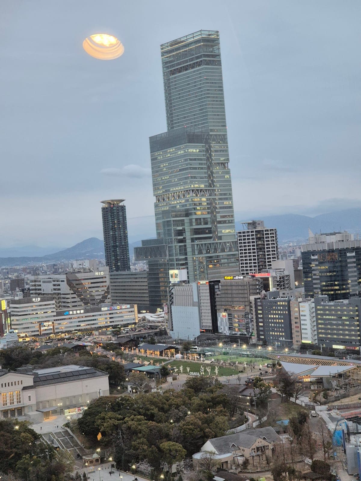 El rascacielos Abeno Harukas visto desde el mirador de la torre Tsutenkaku al atardecer, con el resplandor del sol poniente sobre el horizonte de Osaka