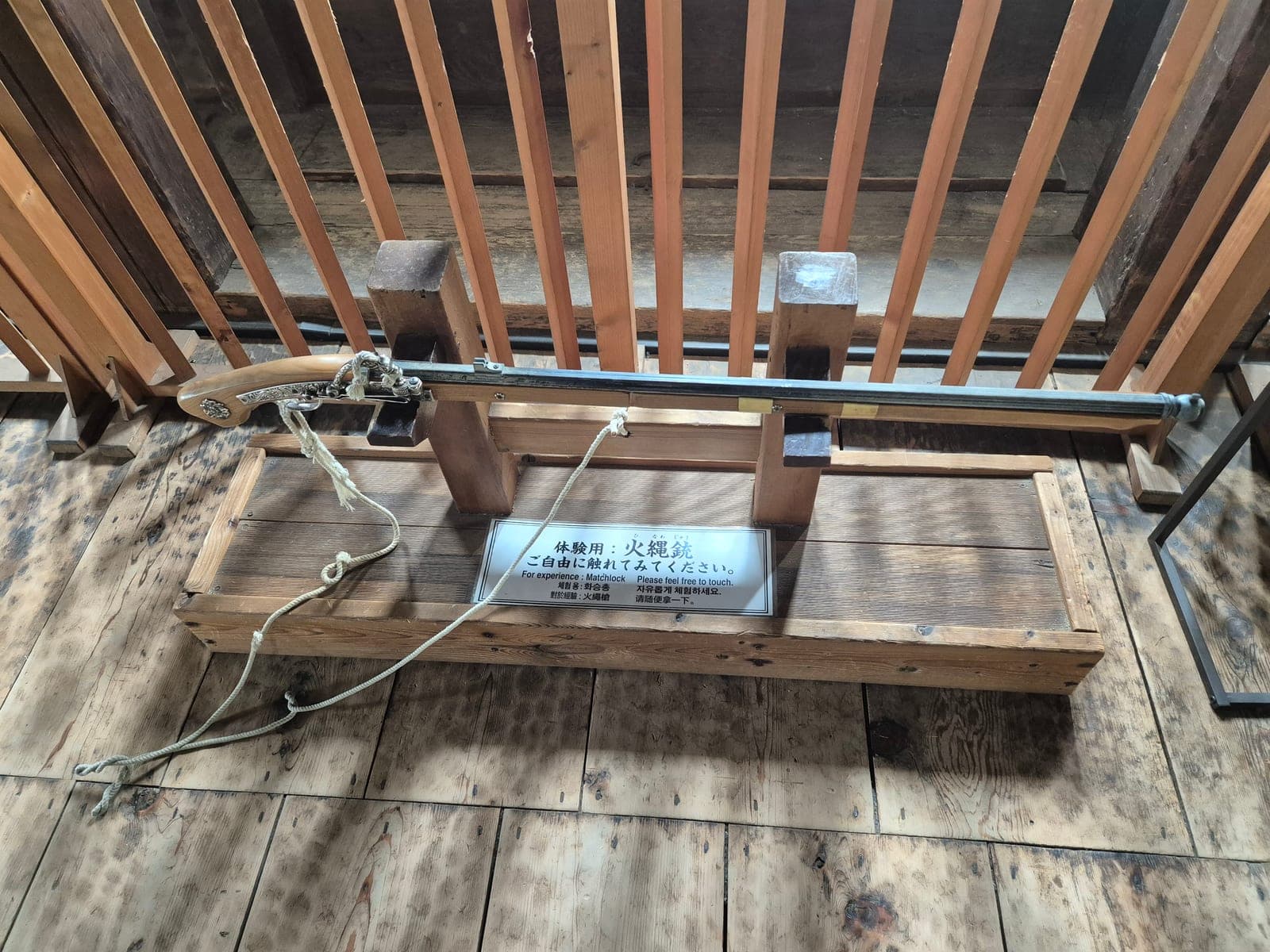 Réplica de un arcabuz tanegashima montada sobre un soporte de madera en Sengan-yagura, con un letrero que invita a los visitantes a tocarla