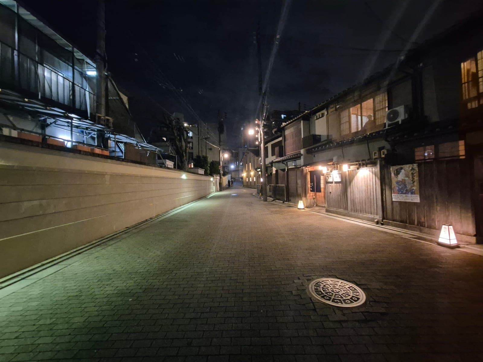 Calle empedrada de Gion de noche con casas de té tradicionales de madera, farolillos encendidos y un cartel con la imagen de una maiko