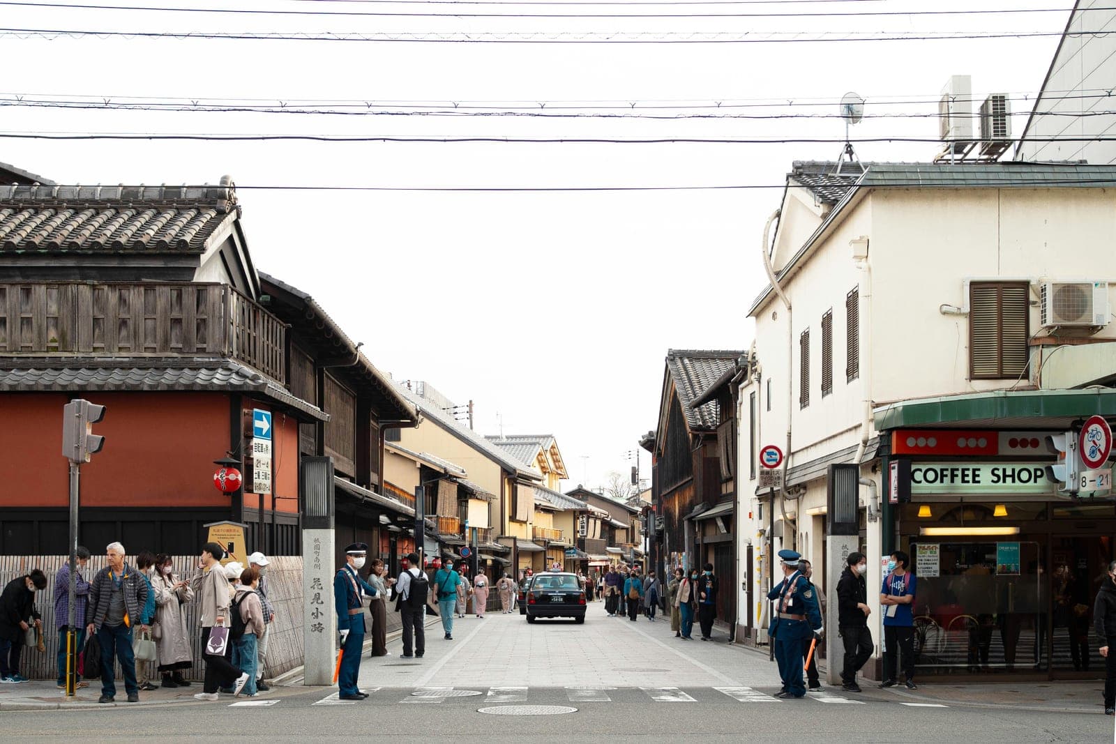 La entrada de Hanamikoji-dori de día, con el marcador de piedra de la calle, casas de té de madera y oficiales guiando a los visitantes