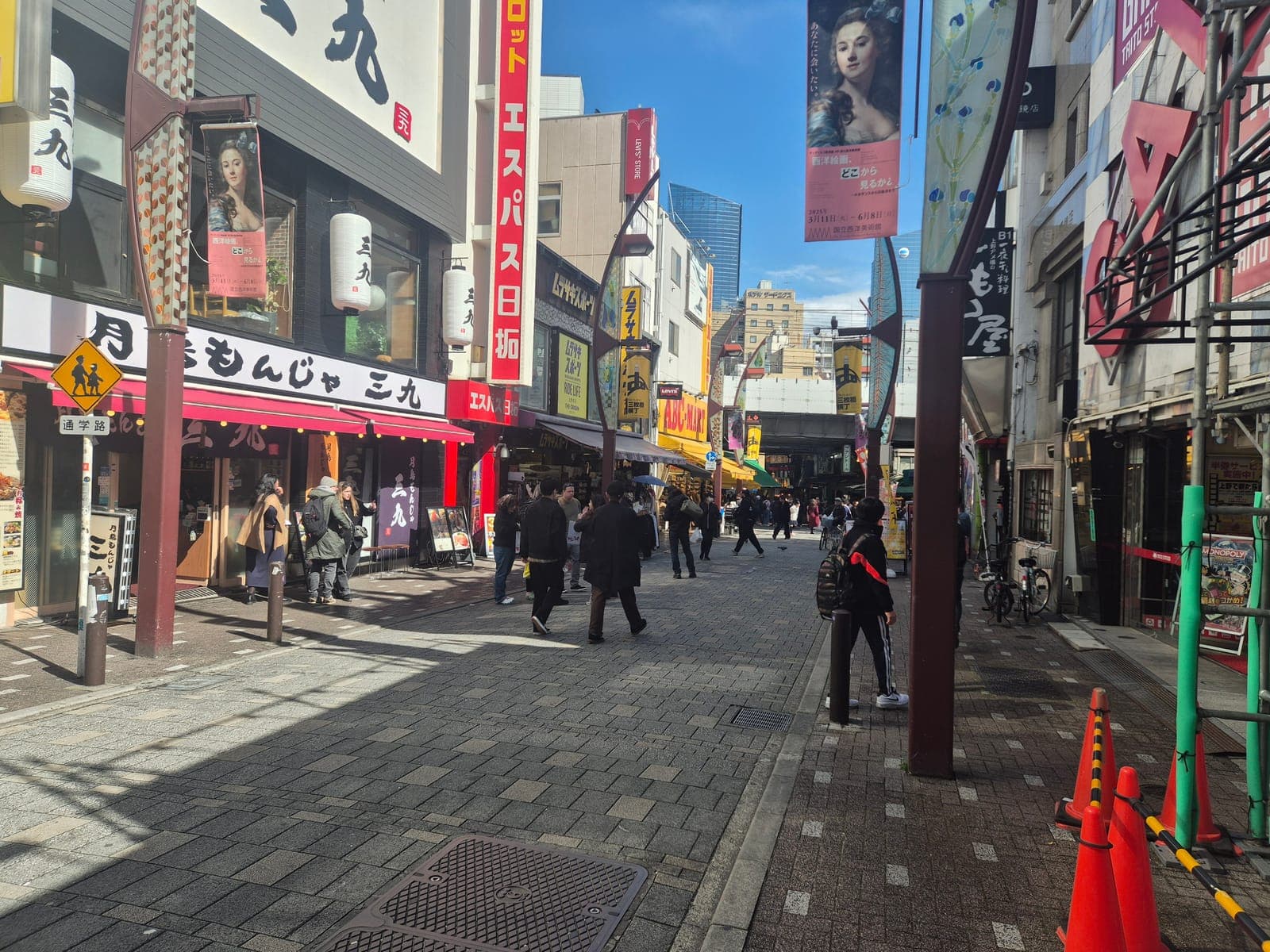 Calle de Ameyoko con letreros de restaurantes, incluido uno de monjayaki, y peatones caminando entre las tiendas