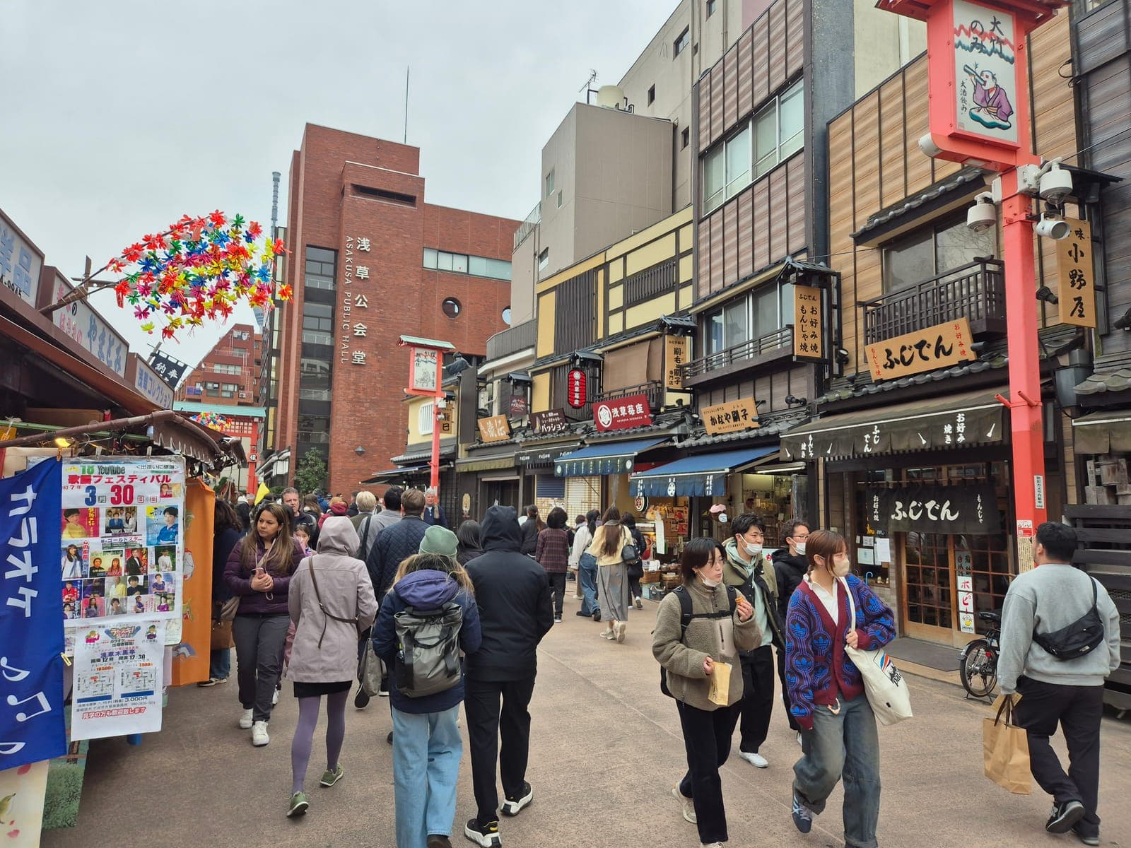 La calle Demboin-dori en Asakusa llena de visitantes, con el edificio Asakusa Public Hall y letreros tradicionales de restaurantes de monjayaki