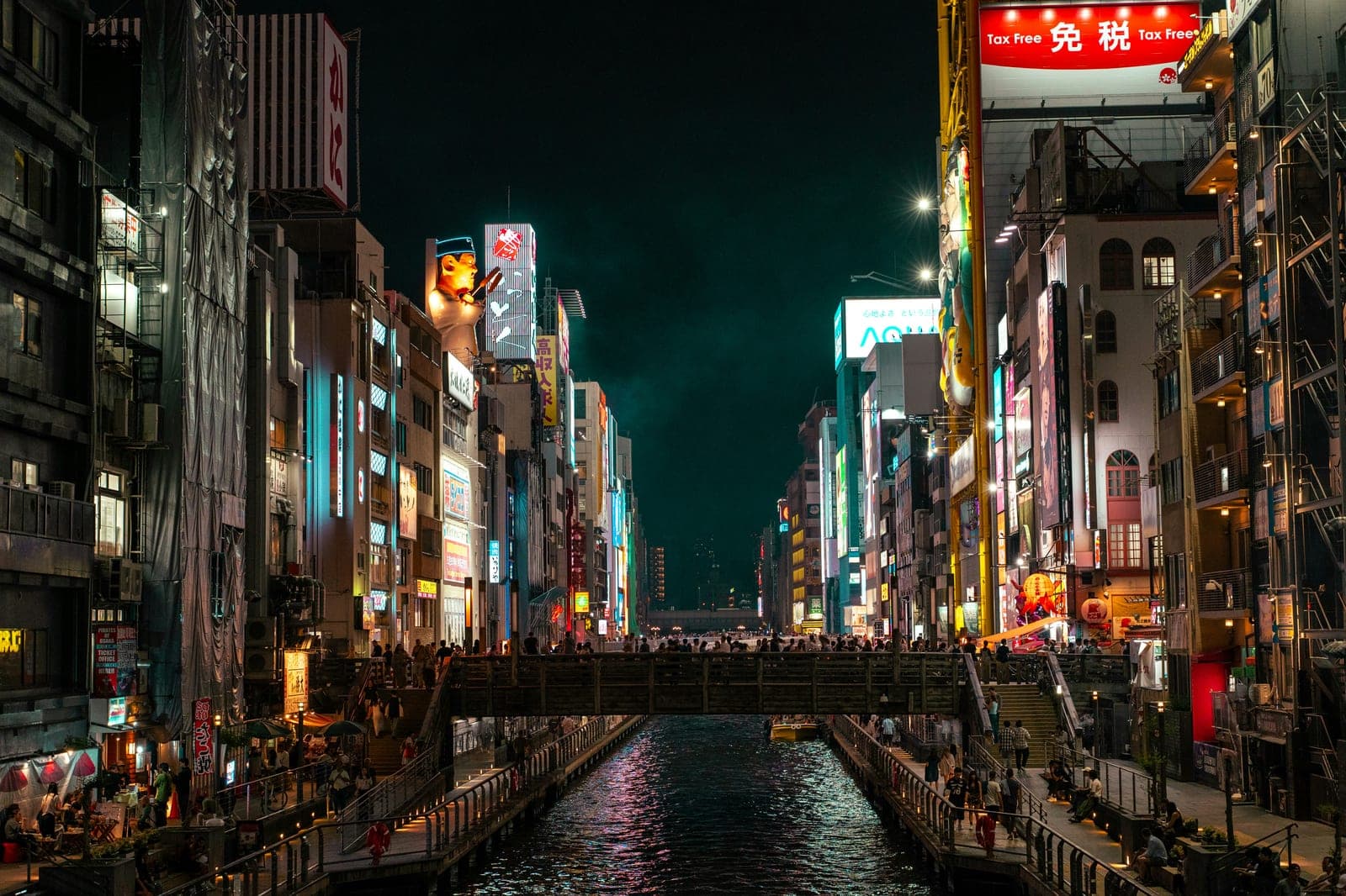 El canal de Dotonbori de noche con el puente Ebisu-bashi lleno de gente y las fachadas cubiertas de letreros de neón a ambos lados