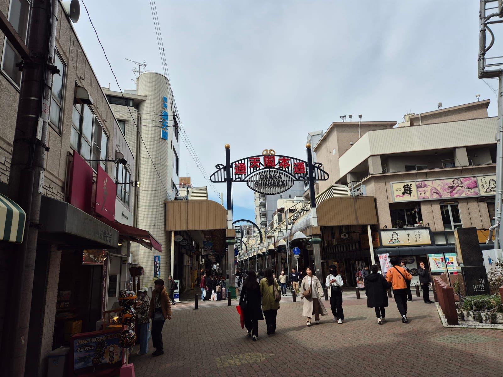 El arco de entrada a la calle Shinsekai Hondori en Osaka, con el letrero 'Osaka Shinsekai' sobre el pasillo comercial techado