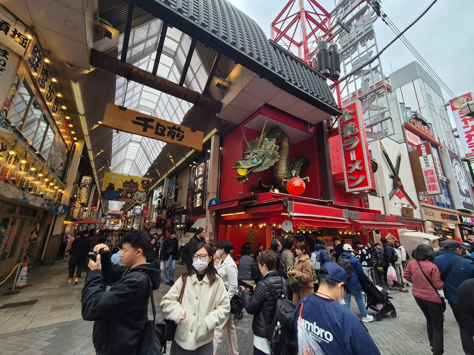 La fachada de Kinryu Ramen en Sennichimae, Osaka, con una escultura de dragón dorado sobre la entrada y gente comiendo en mesas bajas afuera