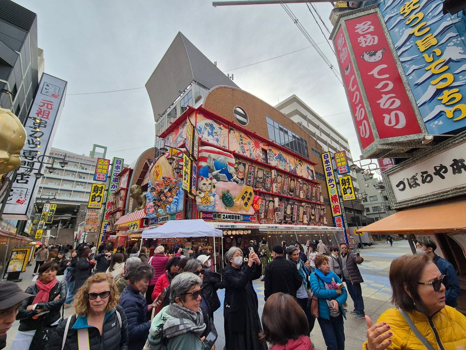 Fachada colorida de un restaurante de kushikatsu en Shinsekai, Osaka, decorada con ilustraciones de sumo, una grulla y un gato de la suerte