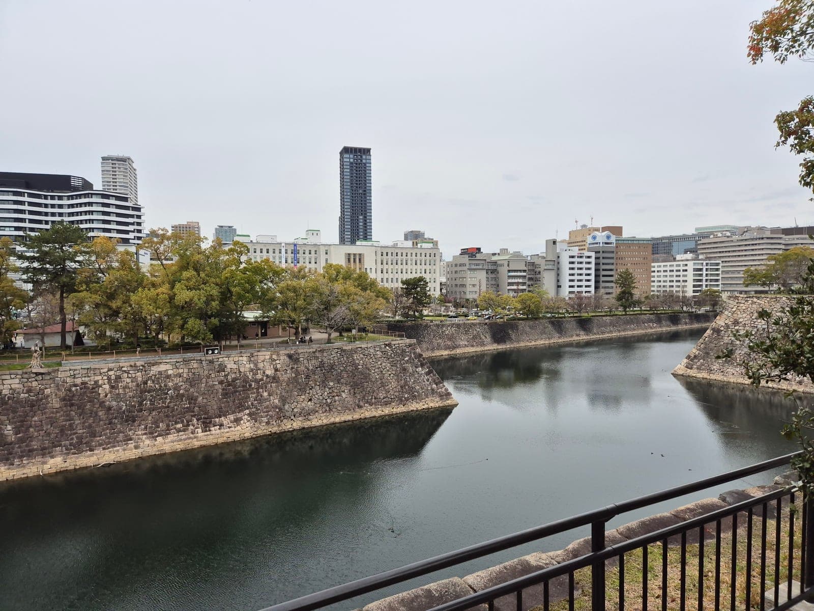 El foso y las murallas de piedra del Castillo de Osaka, con el horizonte de rascacielos de la ciudad al fondo