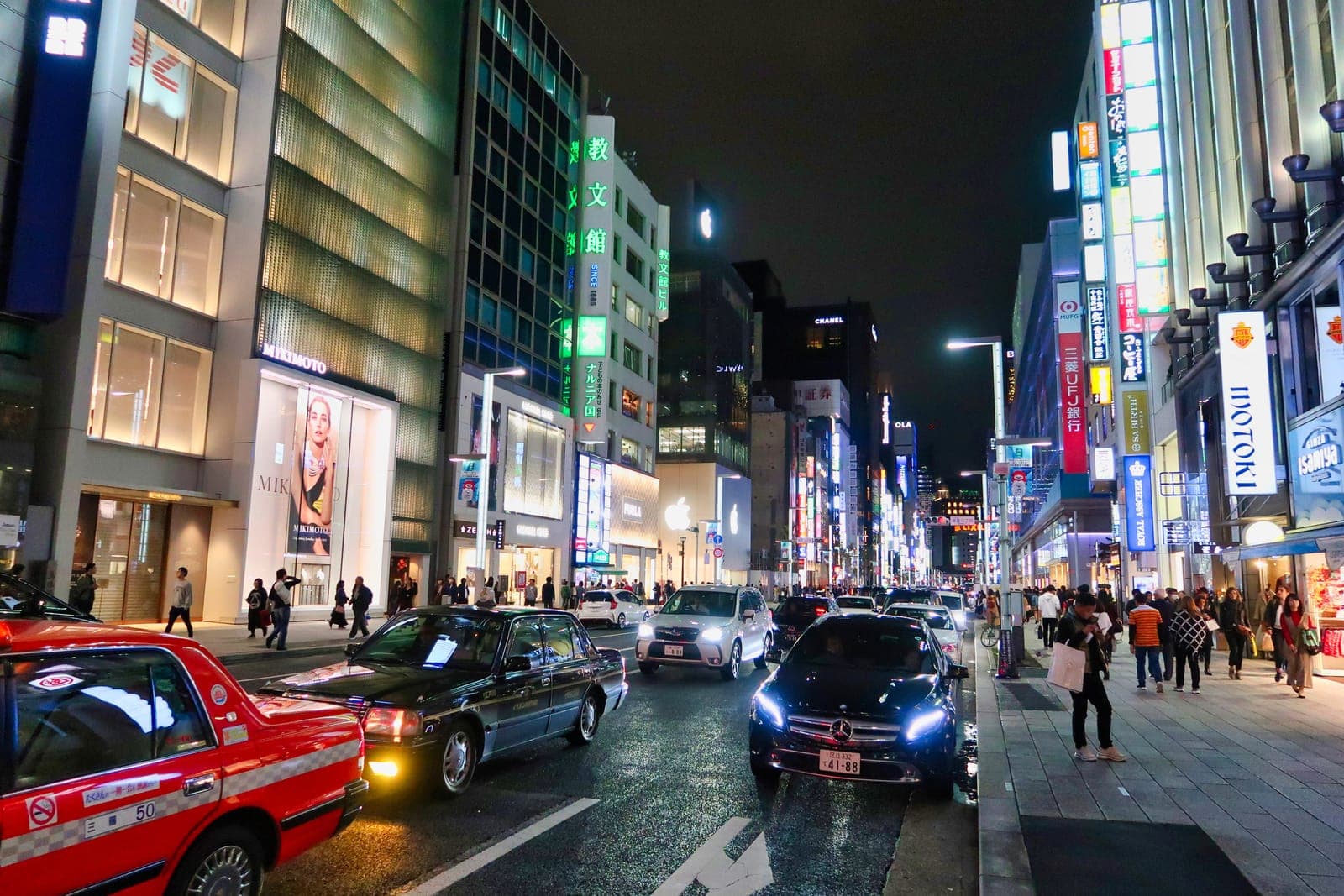 La avenida Chūō-dōri de Ginza de noche, con las boutiques de Chanel, Apple y Mikimoto iluminadas y taxis pasando