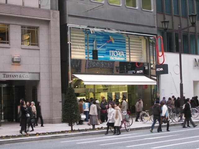 La fachada de la tienda Itoya en Ginza, junto a una tienda de Tiffany & Co., con peatones caminando frente a ambas