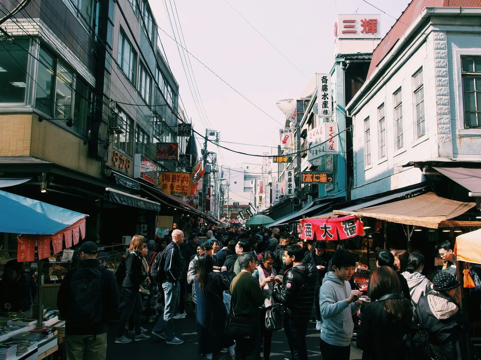 Calle del mercado exterior de Tsukiji con letreros colgantes de puestos de pescado y gente caminando entre las tiendas