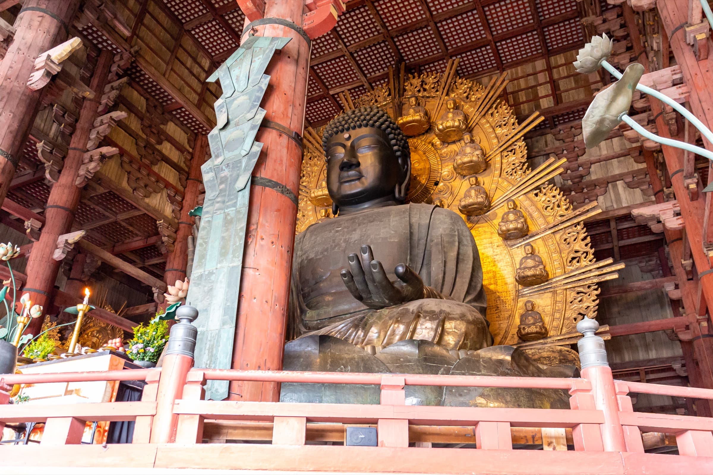 El Gran Buda de bronce del Tōdai-ji visto de frente dentro del Daibutsuden, con el halo dorado de budas pequeños detrás y las columnas rojas del pabellón alrededor