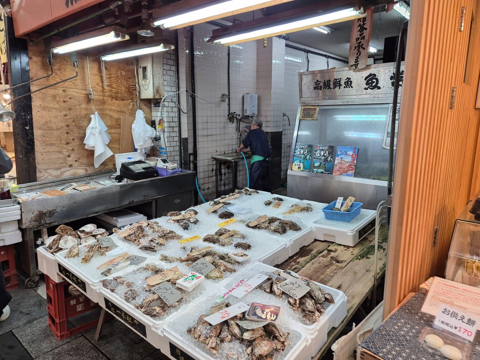 Ostras frescas sobre hielo con etiquetas de precio escritas a mano en un puesto de mariscos de Kuromon Ichiba, Osaka