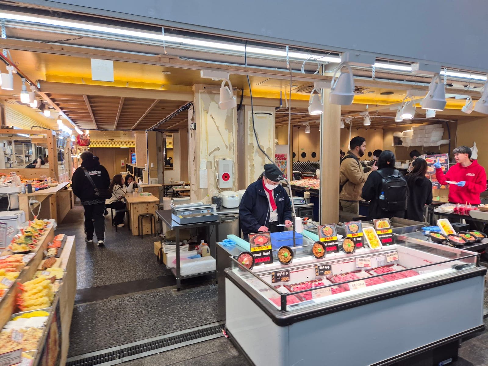 Vitrina refrigerada con cortes de carne wagyu y platillos preparados en un puesto de Kuromon Ichiba, Osaka, con una empleada atendiendo