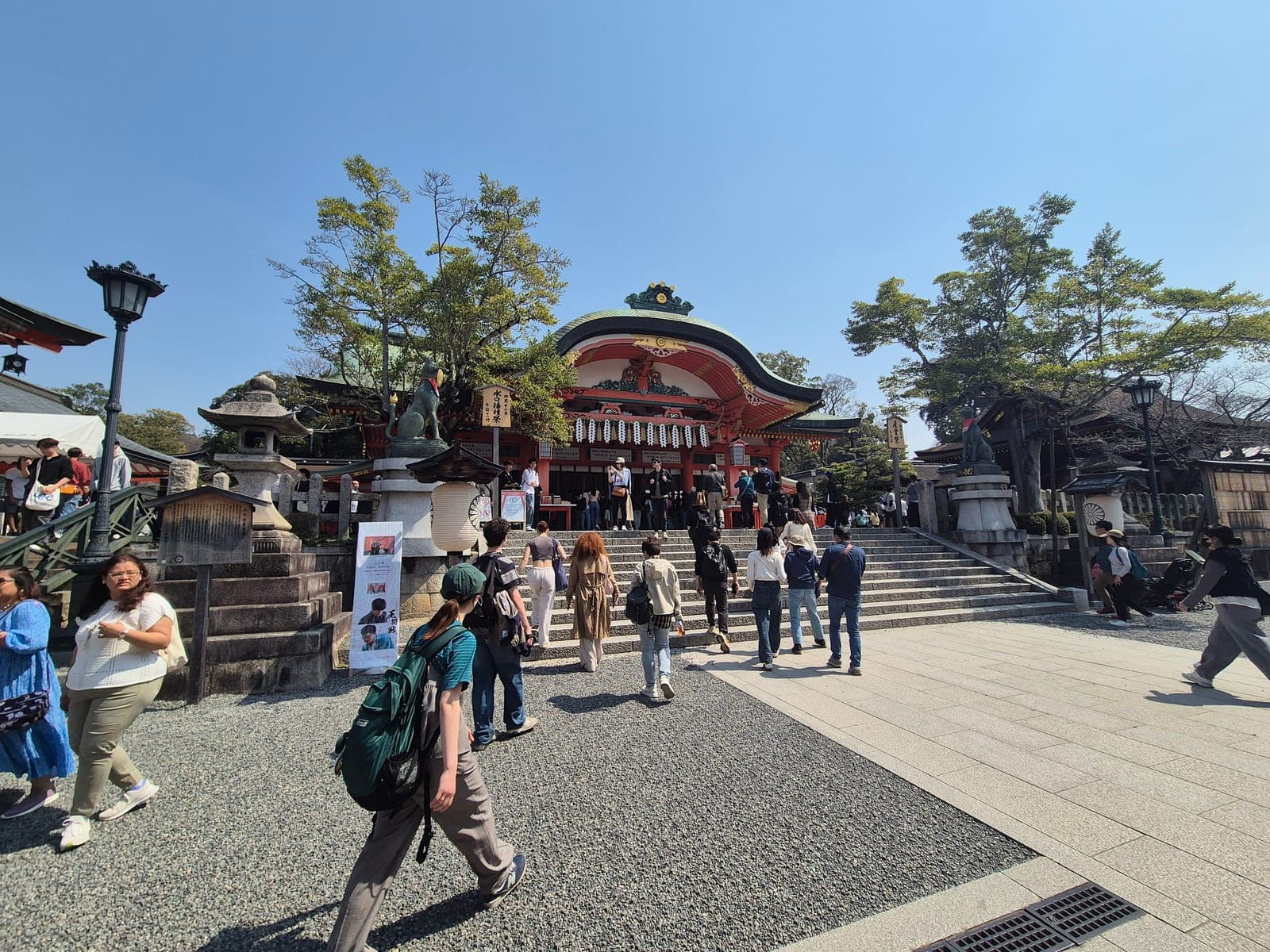 El salón principal del santuario Fushimi Inari Taisha, con techo verde y detalles dorados, y visitantes subiendo las escaleras de piedra