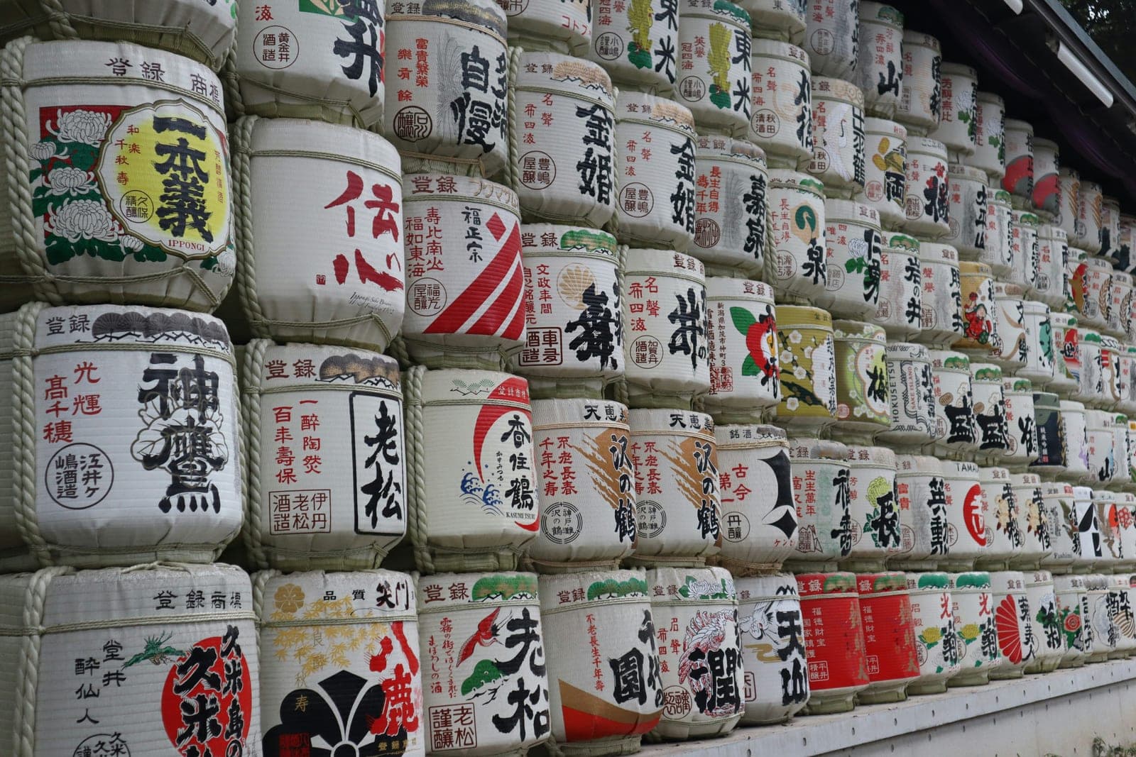 Hileras apiladas de barriles de sake (kazaridaru) envueltos en paja, cada uno con la etiqueta pintada de una casa productora distinta, en el sando del santuario Meiji Jingū